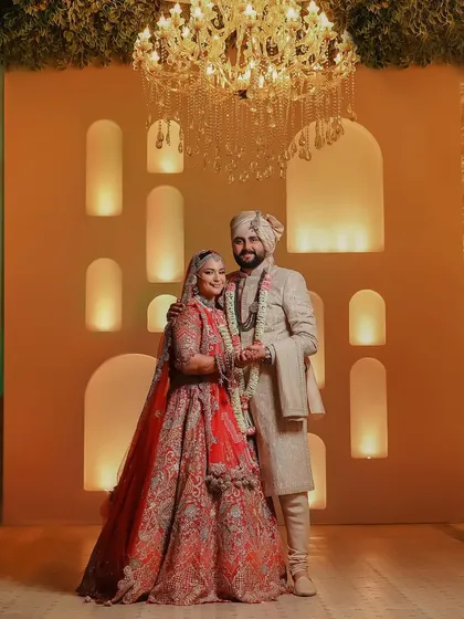 A regal portrait of the couple on their wedding day. The warm, golden light and the grand chandelier create a luxurious and timeless atmosphere.