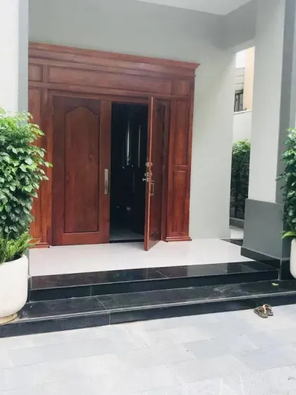 A grand wooden doorway is framed by two large, white planters filled with lush Ficus plants. This simple but effective use of container planting creates a formal and welcoming entrance.