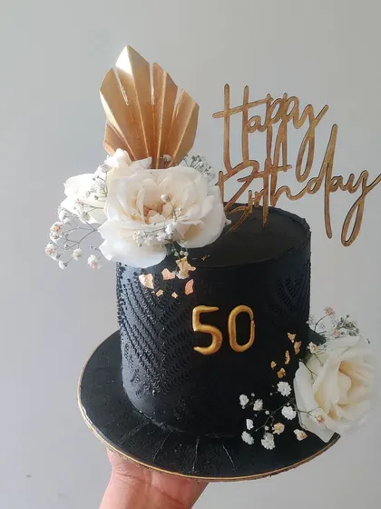 Celebrating a 50th birthday calls for something truly special. This striking black cake features a sophisticated textured pattern, elegant white florals, and gold accents, creating a modern and memorable centerpiece for a milestone celebration.