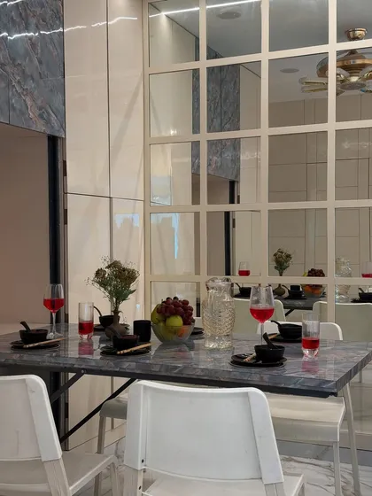 A detailed shot of the dining setup, showing the elegant marble-patterned tabletop against the gridded mirror wall. These details create a feeling of luxury and openness.