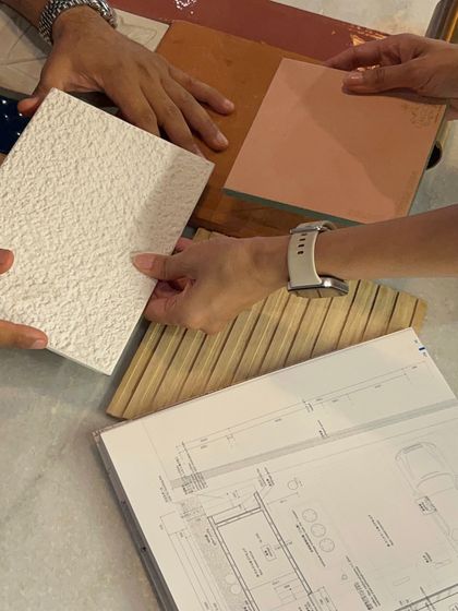 A close-up of our hands collaborating over a mood board, with drawings, wood samples, and textured tiles. This tactile process is where our ideas begin to take physical form.