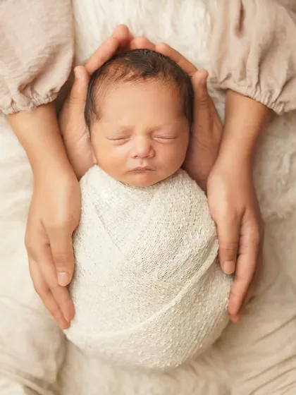 A mother's hands gently cradle her swaddled newborn. This pose emphasizes the feeling of safety and love, creating a powerful memory of how small your baby once was.