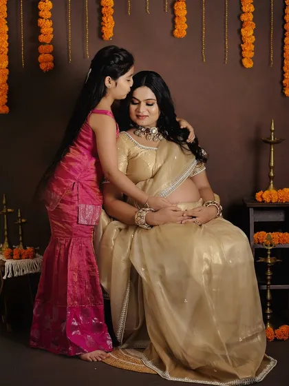 A traditional-themed maternity shoot celebrating culture and family. The mother-to-be looks radiant in a golden saree, sharing a tender moment with her daughter.