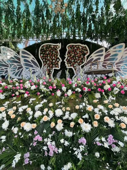 A unique reception backdrop featuring silhouettes of a couple with butterfly wings, surrounded by a garden of fresh flowers.