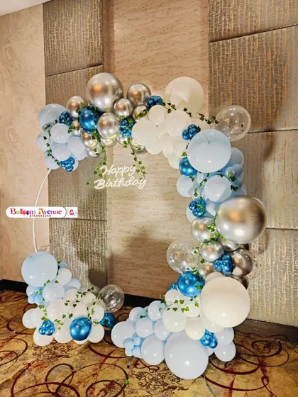 A stylish birthday setup using a square frame with a balloon arch in shades of blue, white, and silver chrome.