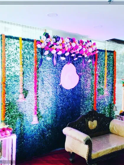 A simple yet elegant baby shower backdrop. A greenery wall is accented with hanging bells and floral strings, with an ornate sofa for the mother-to-be.