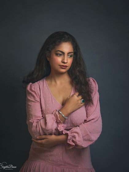 A classic, contemplative pose. This portrait of Divya in a soft pink dress uses a simple, textured background and directional light to create a mood of quiet reflection. The focus is entirely on her expression and the subtle details of her pose.