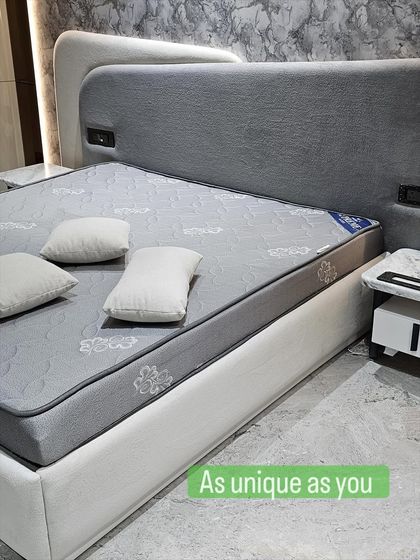 This fully upholstered bed in a soft grey fabric has a unique, multi-layered headboard that adds depth and character. The built-in sockets are a practical touch for modern living.