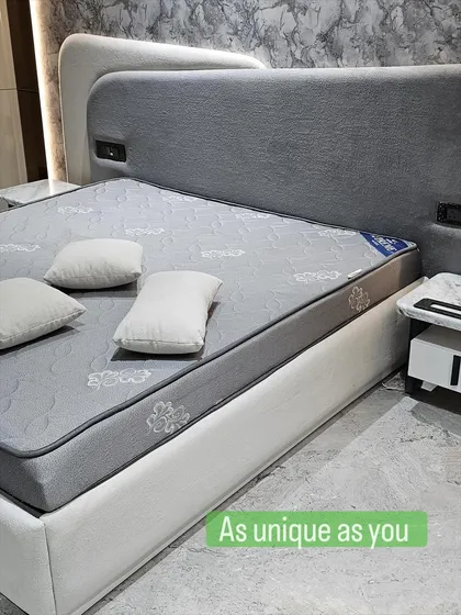 This fully upholstered bed in a soft grey fabric has a unique, multi-layered headboard that adds depth and character. The built-in sockets are a practical touch for modern living.