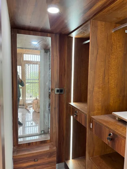 The inside of a walk-in closet we designed, using a rich wood laminate. It includes a full-length mirror, drawers, and vertical profile lighting.