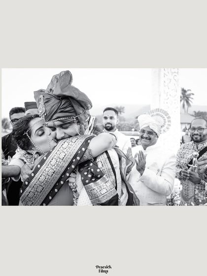 A heartfelt black and white photo of the bride kissing the groom's cheek after their beachside Maharashtrian wedding ceremony.