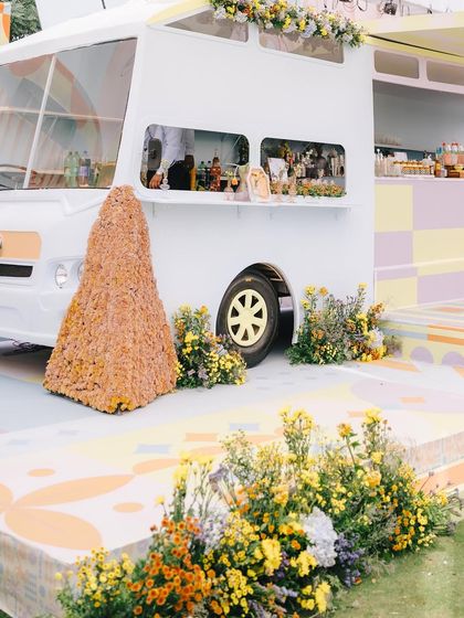 The full view of our custom-built VW bus bar, set on a stage with a hand-painted floor and surrounded by a field of yellow and white flowers.
