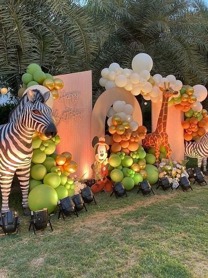 A close-up of the lifelike zebra prop used in an outdoor safari theme, surrounded by a lush arrangement of green and orange balloons.