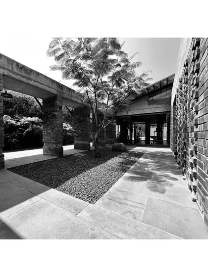 A black-and-white photo of a courtyard passage, where the texture of a projecting brick wall contrasts with smooth stone flooring. The play of light and shadow animates the space.