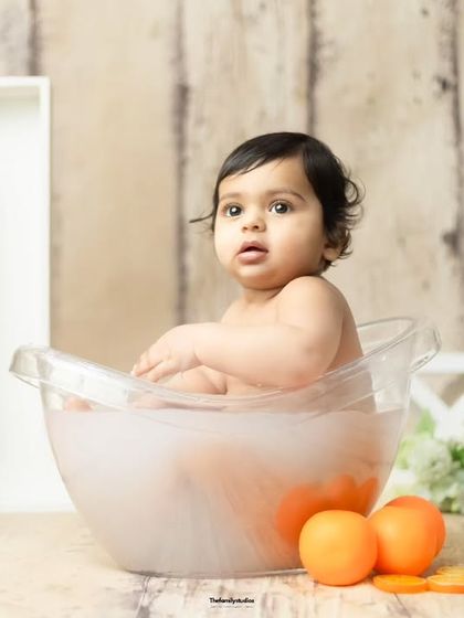 A calm moment in an orange-themed milk bath, set against a rustic wooden backdrop for a first birthday.