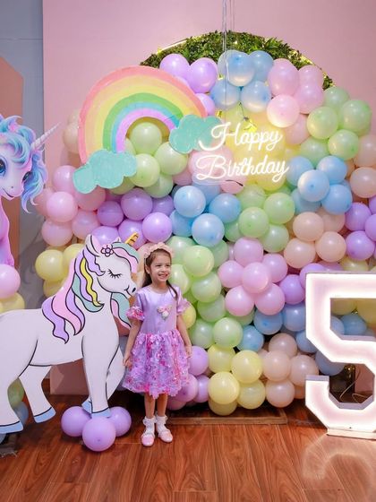 The birthday girl stands in front of her spectacular unicorn and rainbow birthday backdrop, a truly magical setting for her 5th birthday.
