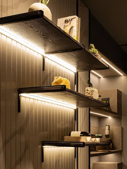 We use lighting to accentuate architectural details. Here, LED strips are concealed beneath each shelf, highlighting the texture of the grooved back panel and casting a soft, ambient light on the decorative items.