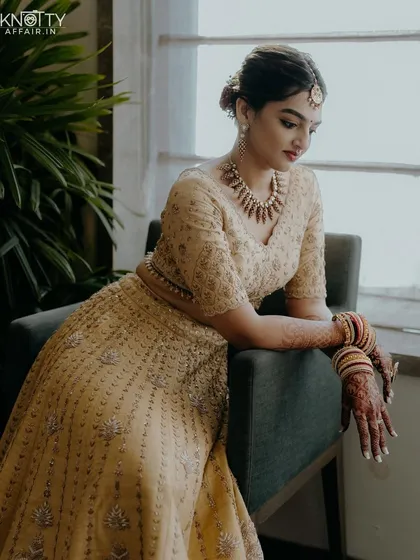An elegant bridal portrait from a beach wedding. The bride, dressed in a beautiful golden lehenga, is captured in a moment of quiet reflection by the window, with soft, natural light highlighting her features.