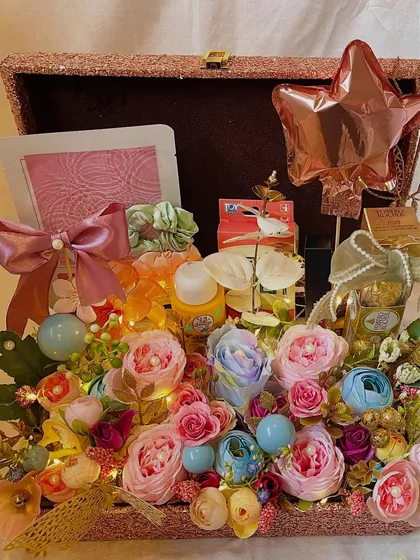 The full view of the floral trunk hamper, packed with skincare goodies, scrunchies, and chocolates nestled among a garden of flowers. A star shaped balloon adds a celebratory touch.