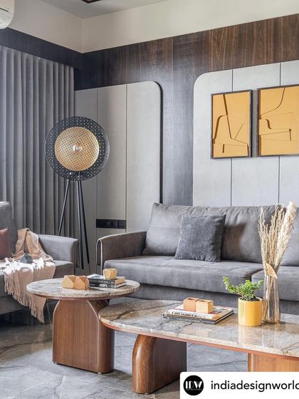 The living area of Rustic Reverie is designed for comfort and style. The grey sofa is complemented by warm yellow artwork and a statement floor lamp, creating a balanced composition of color, texture, and light.