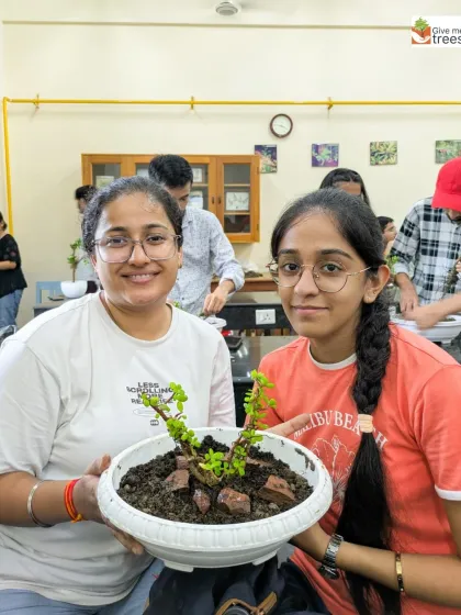 Two students proudly show off their newly created bonsai. This workshop gives them a living piece of art to care for, teaching them about long-term plant maintenance.