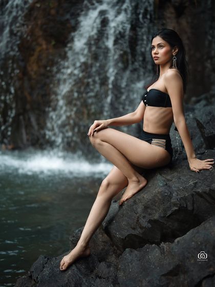A serene and thoughtful pose, with the model sitting on a rock by the waterfall. The soft, natural light and the sound of the water create a peaceful and meditative mood.