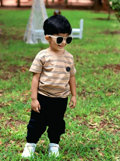 A cool toddler in sunglasses smiles during his second birthday outdoor shoot, capturing a candid and stylish moment.
