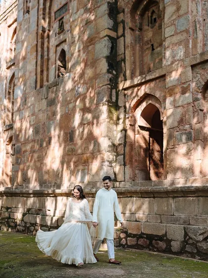 A happy, candid shot of a couple walking hand-in-hand through a park, the bride's dress flowing.