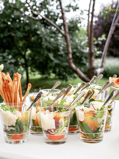 An outdoor buffet table with salad cups and breadsticks. This setup is perfect for a garden party or a daytime wedding event, offering light and refreshing options for guests to enjoy in a beautiful setting.