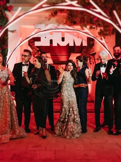 The happy couple and their family pose under a neon archway, capturing the electric energy and joy of the 'London Underground' themed cocktail night.