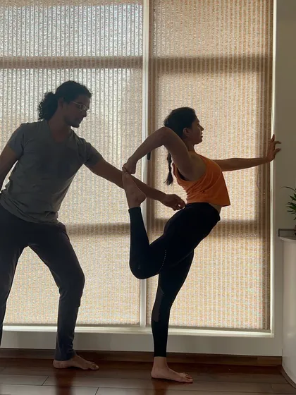 A student receives an adjustment in Natarajasana, the Lord of the Dance pose. This assistance helps with balance and achieving a deeper backbend, embodying the grace and strength of the asana.
