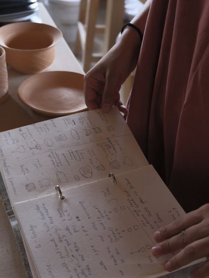 The journey of a professional potter is documented in sketchbooks and plans. Here, a student reviews their designs and notes, a crucial part of the collection planning process in our immersive course.