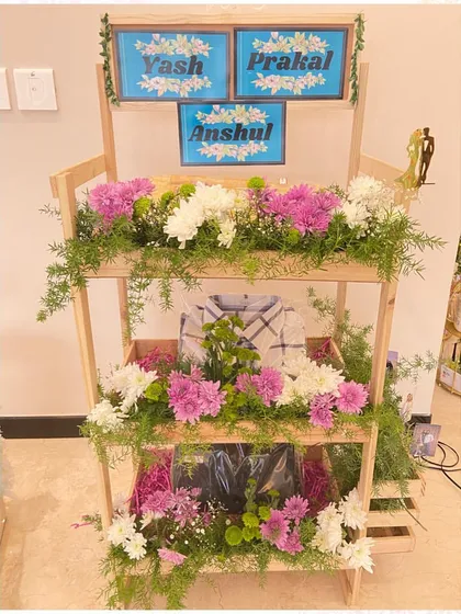 A multi-tier floral shelf for a groom's trousseau. This personalized wooden stand beautifully displays gifts for the groom and his family, decorated with an abundance of fresh flowers.