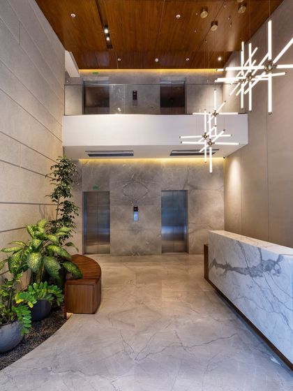 This apartment lobby is a statement of quiet luxury. The double-height space is grounded by a dramatic marble reception desk and complemented by warm wood ceilings and lush greenery, creating a balanced and elevated arrival experience.