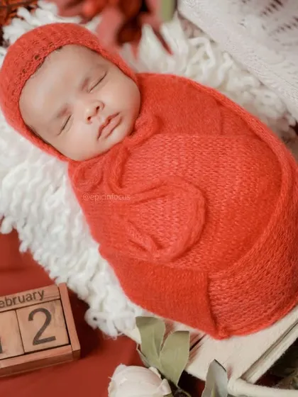 A close-up of the baby in the red swaddle, with a calendar block marking a special date.