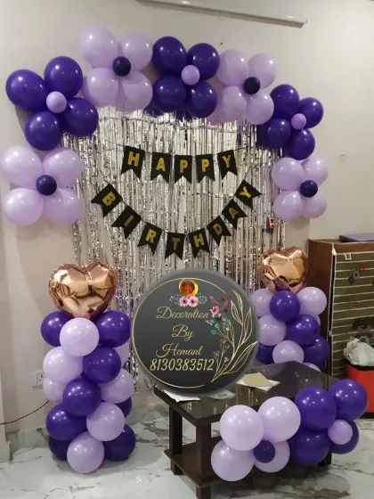A birthday decoration in shades of purple. This setup features a silver fringe backdrop, a "Happy Birthday" banner, and an arch of dark and light purple balloons, perfect for a celebration in a smaller space.