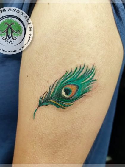 A small but vibrant peacock feather tattoo on the arm. We packed in the iconic green, blue, and gold colors to make it look realistic and bright.
