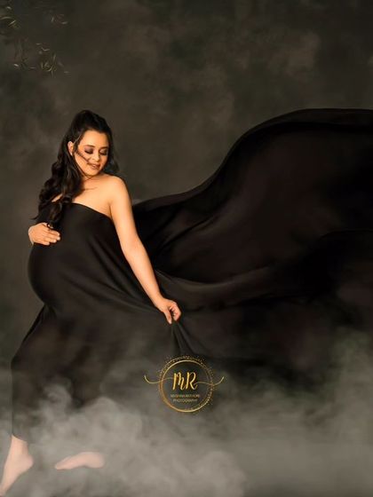 A dreamy and atmospheric portrait. The mother-to-be is surrounded by mist and a floral arch, with black fabric flowing around her for a dramatic effect.