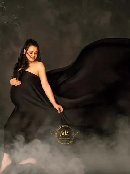 A dreamy and atmospheric portrait. The mother-to-be is surrounded by mist and a floral arch, with black fabric flowing around her for a dramatic effect.