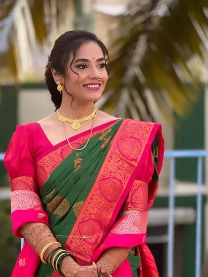 A bride in a green and pink saree, ready for her wedding. The makeup is soft and natural, with a simple hairstyle that adds to the elegance.