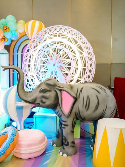 A large elephant prop in front of a lit-up ferris wheel, part of the pastel carnival's charming decor.