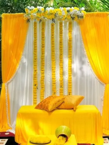 This is a beautiful and simple Haldi decor setup, perfect for a home or garden function. I used bright yellow and white drapes with hanging marigold garlands to create a fresh and traditional photo corner.