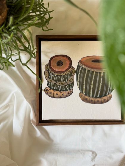 A peek at a miniature painting of a tabla set, seen through the leaves of a plant. This composition connects the art to a sense of home and nature.