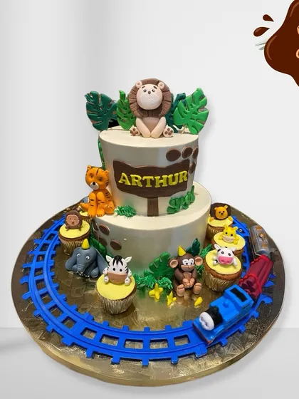 This jungle-themed cake set includes a two-tier cake and matching animal cupcakes. The entire display is set on a train track with a toy train, combining two popular themes in one.
