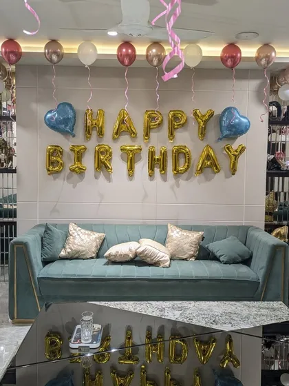 Even a simple living room can be transformed for a celebration. This classic setup includes "Happy Birthday" foil letters on the main wall, with helium balloons in rose gold, pink, and white floating on the ceiling to fill the space with color.