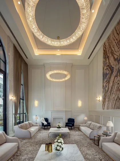 This formal drawing room in The Grand Alabaster is a showcase of neoclassical luxury. The double-height space is anchored by two large, ring-shaped crystal chandeliers and a monumental art piece, creating an environment of pure sophistication.