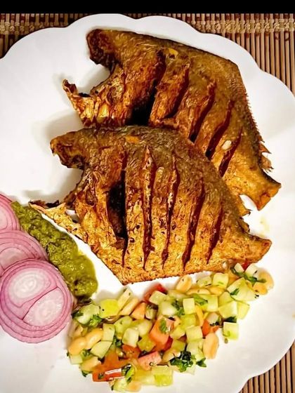 Two beautifully fried pomfret fish, served with a side of kachumber salad and sliced onions. A delicacy for seafood lovers.