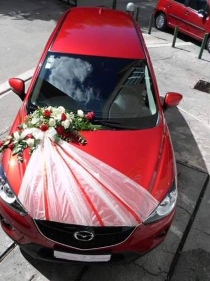 A minimalist and modern car decoration for a red car, using a simple bouquet of white and red roses with a white fabric drape.