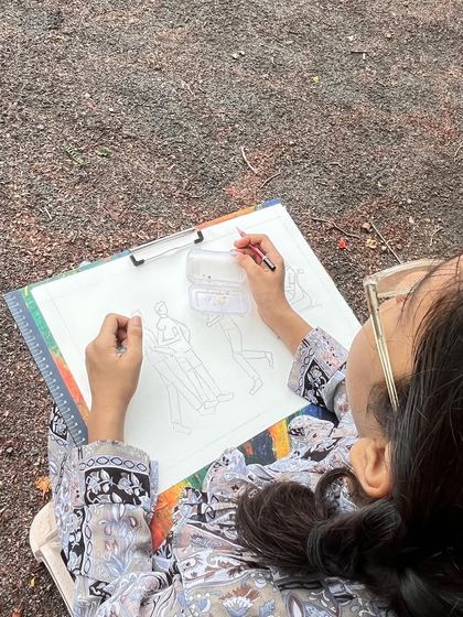 An over-the-shoulder view of a student mapping out the basic shapes and poses of people in the park. This initial step is crucial for getting the composition right before adding details.