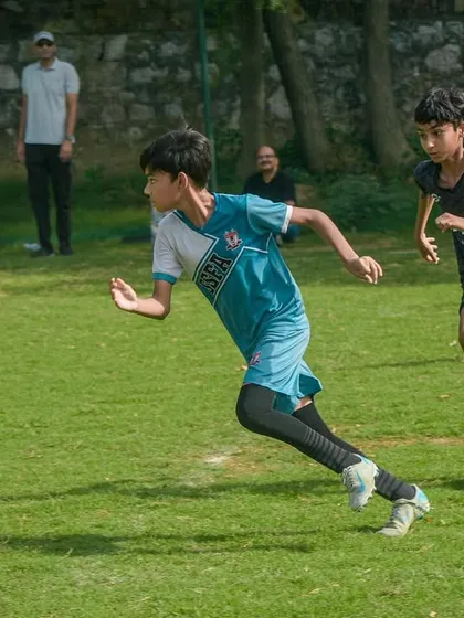 A young player sprints with the ball down the field, demonstrating speed and determination while being pursued by a defender.